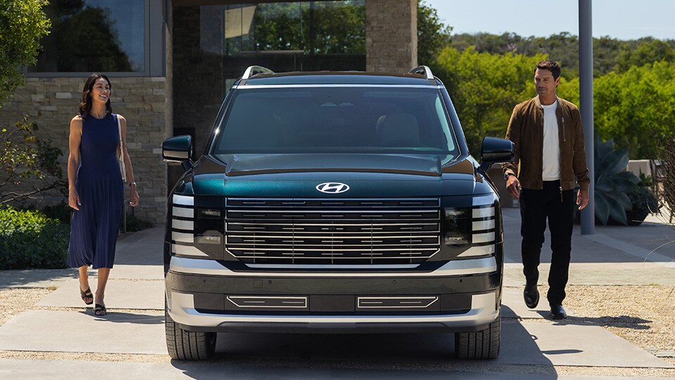 Woman and man standing on opposite sides of a 2026 Palisade